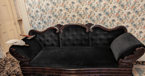 A vintage black velvet couch with ornate wooden details, set against a floral wallpaper background.
