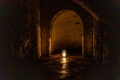A dimly lit stone corridor with an archway, featuring a lantern casting light on the floor.