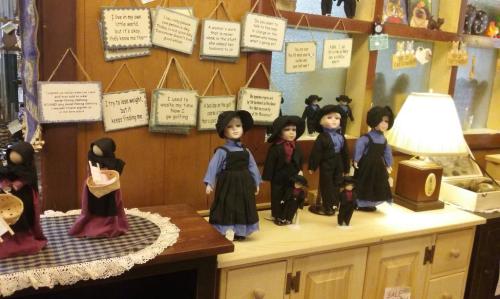 A display of dolls in traditional clothing, with decorative signs and a lamp on a wooden shelf.