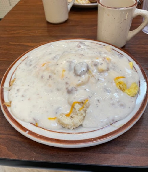 A plate of biscuits covered in creamy sausage gravy, with a side of coffee in a mug.
