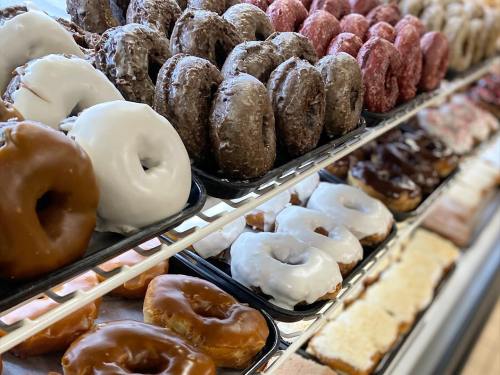 A display of assorted donuts, including glazed, chocolate, and frosted varieties, arranged on trays.