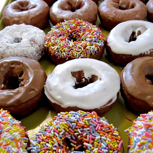 A variety of donuts, including glazed, chocolate, and sprinkled, arranged on a yellow platter.