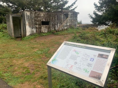A weathered concrete structure beside an informational sign about World War II, surrounded by greenery and trees.