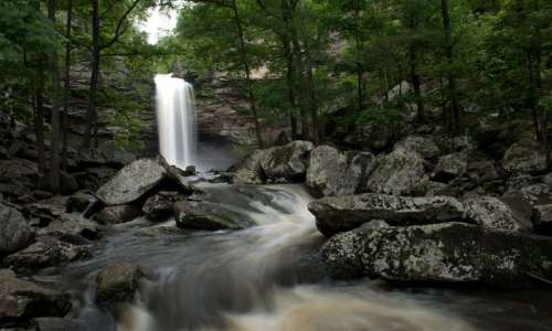 A serene waterfall cascades down rocky cliffs, surrounded by lush green trees and a flowing river.
