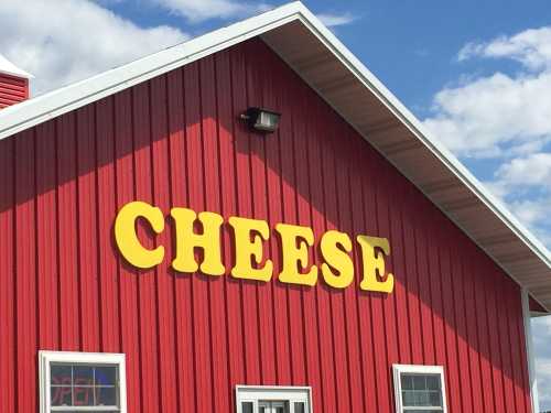 Red barn with a yellow sign that reads "CHEESE" against a blue sky with clouds.