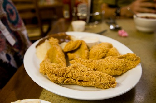 A plate of golden-brown fried fish fillets with sides of dipping sauces and mashed potatoes.