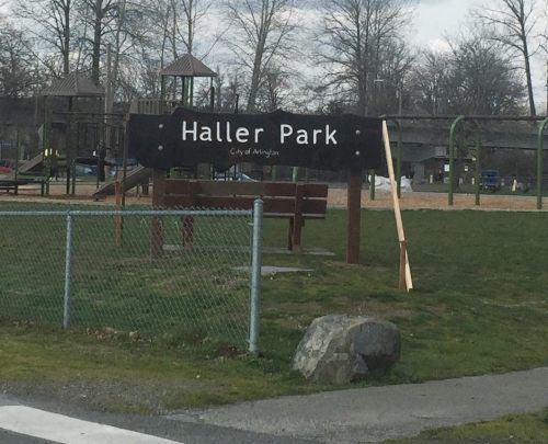 Sign for Haller Park in Arlington, featuring playground equipment and grassy areas in the background.