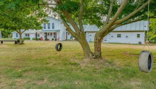 A white house with a blue roof surrounded by trees and a grassy yard, featuring a tire swing hanging from a tree.