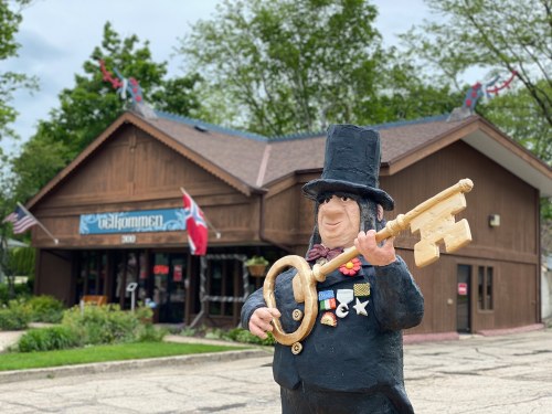 A statue of a man in a top hat holding a large key stands in front of a wooden building with flags and decorations.