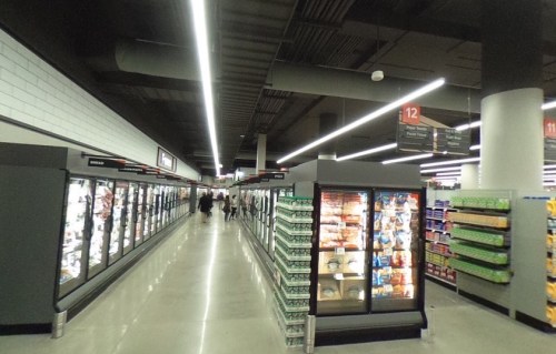 A spacious grocery store aisle with freezer sections on both sides and shelves stocked with various products.