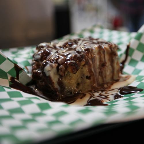 A decadent dessert slice drizzled with chocolate sauce on a green and white checkered paper.