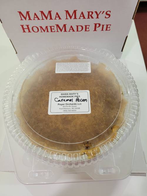 A pecan pie in a clear plastic container, labeled "Mama Mary's Homemade Pie," placed on a white surface.