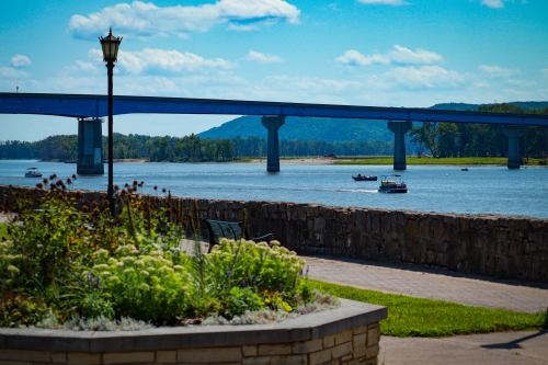 A scenic view of a river with boats, a bridge in the background, and a landscaped area in the foreground.