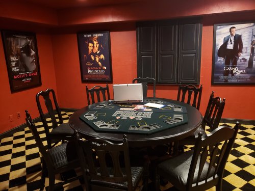 A poker table surrounded by chairs, with movie posters on the walls and a checkered floor.