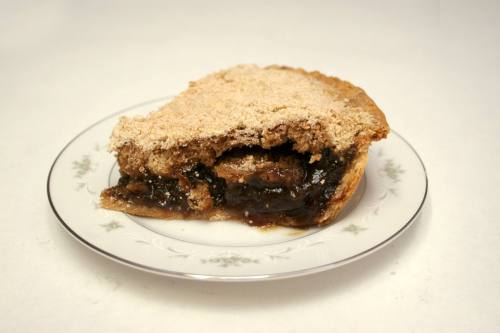 A slice of pie with a crumbly topping on a decorative plate, revealing a dark, gooey filling inside.