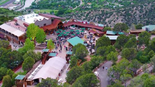 Aerial view of a lively outdoor venue with green tables, surrounded by trees and hills.