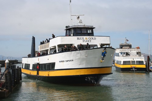 A ferry named "Harbor Emperor" approaches a dock, with passengers on board and another ferry in the background.