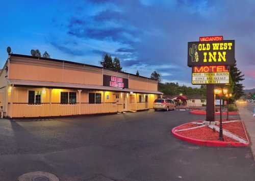 A motel named "Old West Inn" with a neon sign, surrounded by trees and a parking lot at dusk.