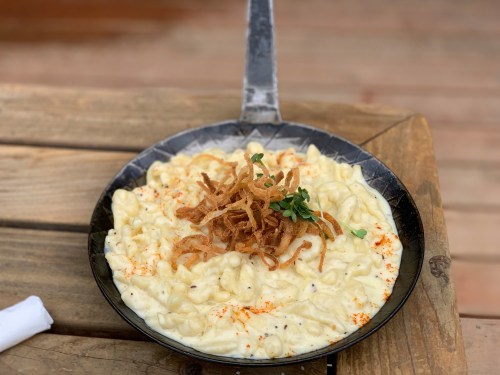 Creamy macaroni and cheese topped with crispy fried onions, served in a black skillet on a wooden table.