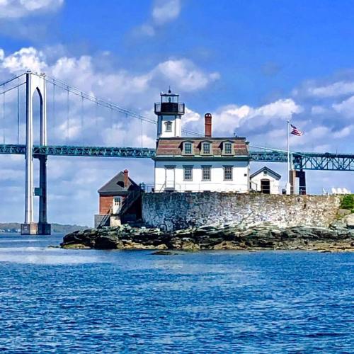 A scenic view of a lighthouse on a rocky shore with a bridge and blue sky in the background.
