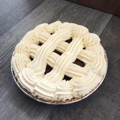 A round pie with a lattice design of creamy frosting on top, resting on a wooden surface.