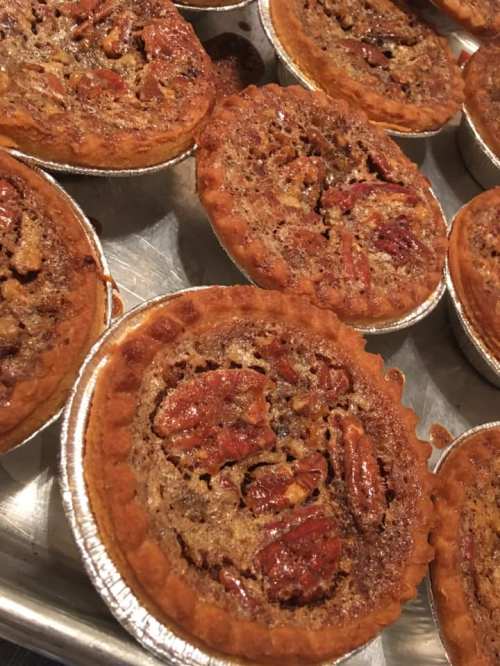 A tray of mini pecan pies with golden crusts and shiny, nut-filled tops.