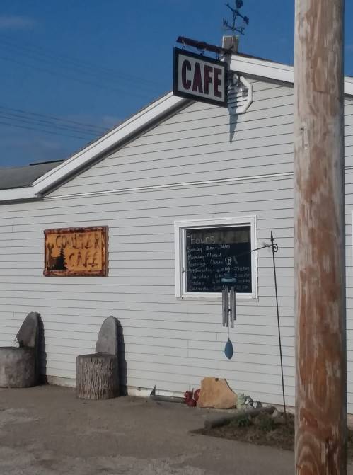 A small café building with a sign, featuring a menu board and rustic decor outside.