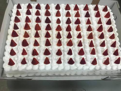 A large rectangular cake topped with rows of whipped cream and small red strawberry pieces.