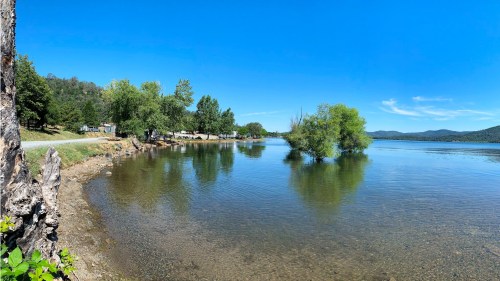 A serene lake scene with clear water, trees along the shore, and a blue sky in the background.