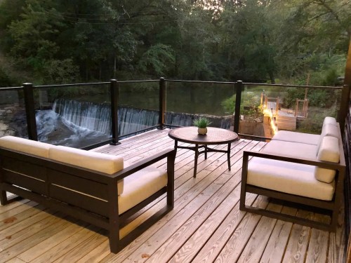 A cozy outdoor deck with seating, overlooking a serene waterfall and lush greenery.