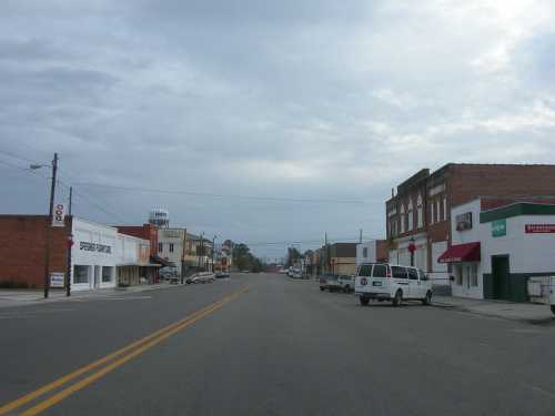 A quiet street in a small town, lined with shops and buildings under a cloudy sky.