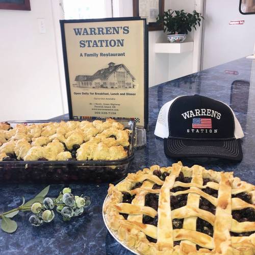 A display of pies and a cap in front of a sign for Warren's Station, a family restaurant open for meals daily.