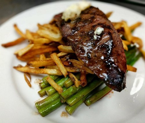 A plate featuring grilled steak on a bed of green beans, topped with butter, alongside crispy French fries.