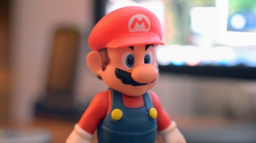 A close-up of a Mario figurine wearing a red hat and blue overalls, with a blurred background.