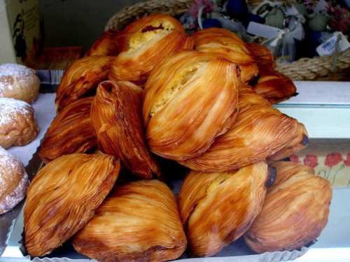 A pile of golden, flaky pastries with a crispy texture, displayed in a bakery window.