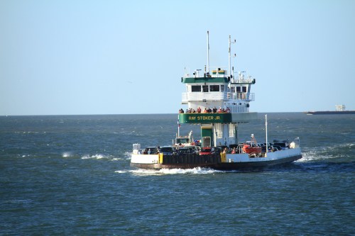 A ferry boat named "RAY STOKER JR" navigates through calm waters, with passengers visible on the upper deck.