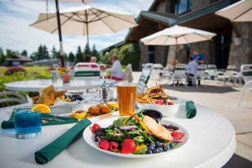 A table set outdoors with colorful salads, drinks, and umbrellas, with people dining in the background.