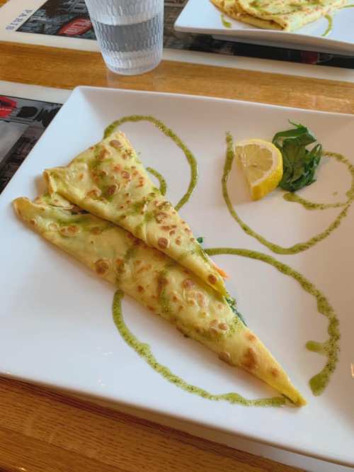 Two folded crepes on a white plate, garnished with lemon and a green sauce swirl.