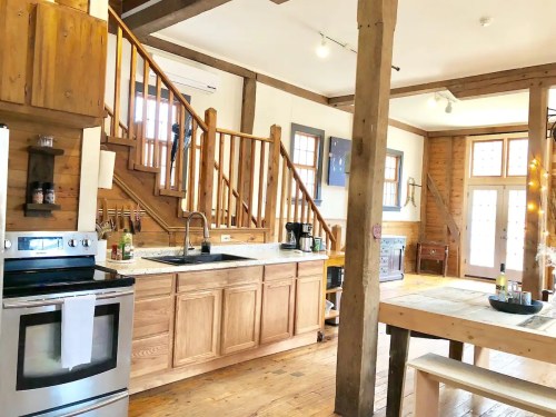 A cozy kitchen with wooden beams, a marble countertop, and a staircase leading to an upper level. Bright and inviting space.