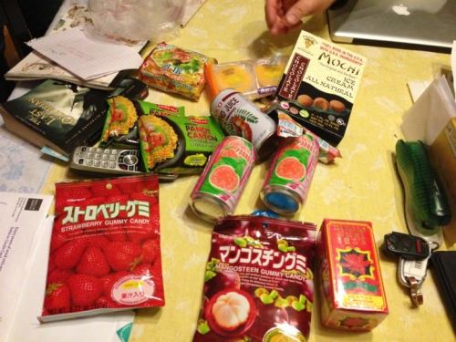 A cluttered table with various snacks, drinks, and a phone, including gummy candies and mochi packaging.