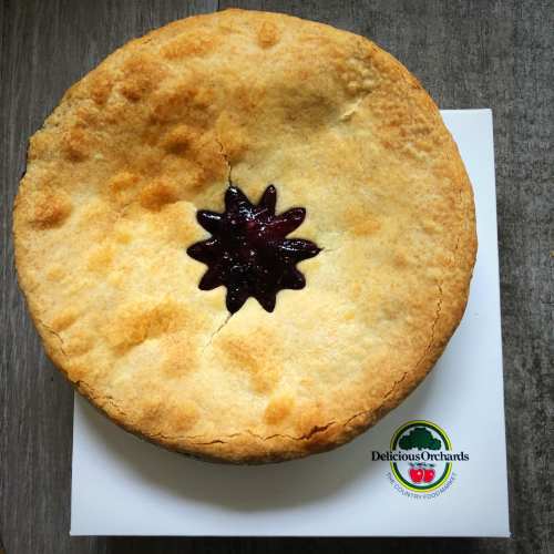 A golden-brown pie with a star-shaped fruit filling on a white plate, featuring a logo for Delicious Orchards.