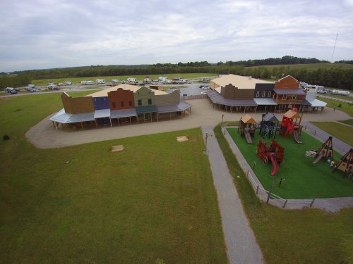 Aerial view of a western-style town with colorful buildings and a playground, surrounded by green grass and trees.