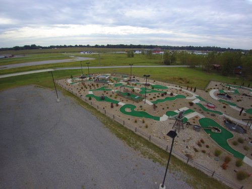 Aerial view of a mini-golf course with green turf, pathways, and scattered landscaping, set in an open area.