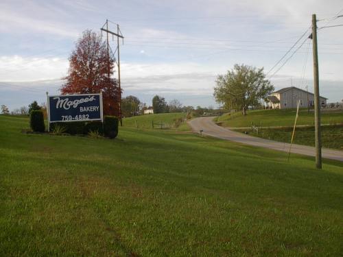 Sign for McGee's Bakery beside a rural road, with green grass and trees in the background under a cloudy sky.