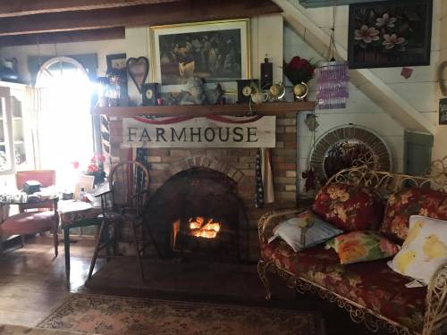 Cozy farmhouse interior with a brick fireplace, floral couch, and rustic decor, creating a warm, inviting atmosphere.