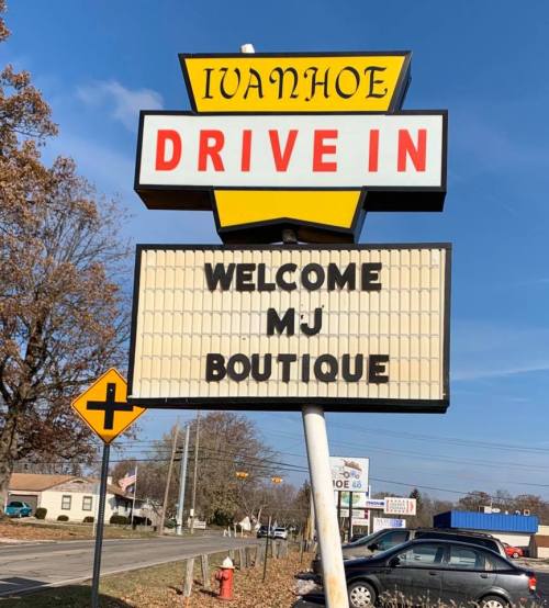 Sign for Ivanhoe Drive-In featuring "Welcome MJ Boutique" against a clear blue sky.