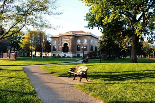 A park scene featuring a path, a bench, and a historic building surrounded by trees and greenery.