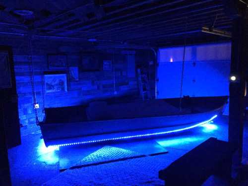 A boat in a dimly lit garage, illuminated by blue LED lights along its edge.