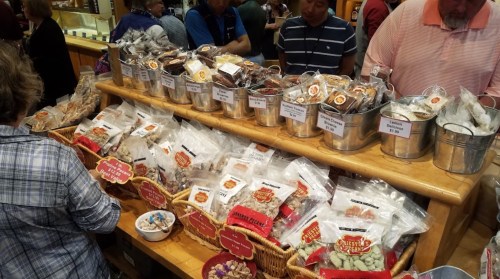 A busy market stall displaying various packaged snacks in baskets and buckets, with customers browsing.
