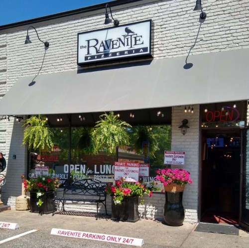 Exterior of Ravenite Pizzeria with a welcoming "Open" sign and vibrant flower planters.